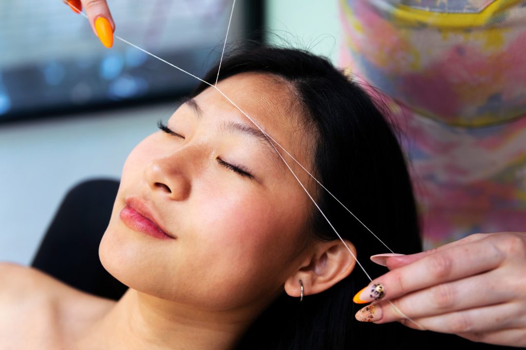 beautician performs eyebrow threading on a woman