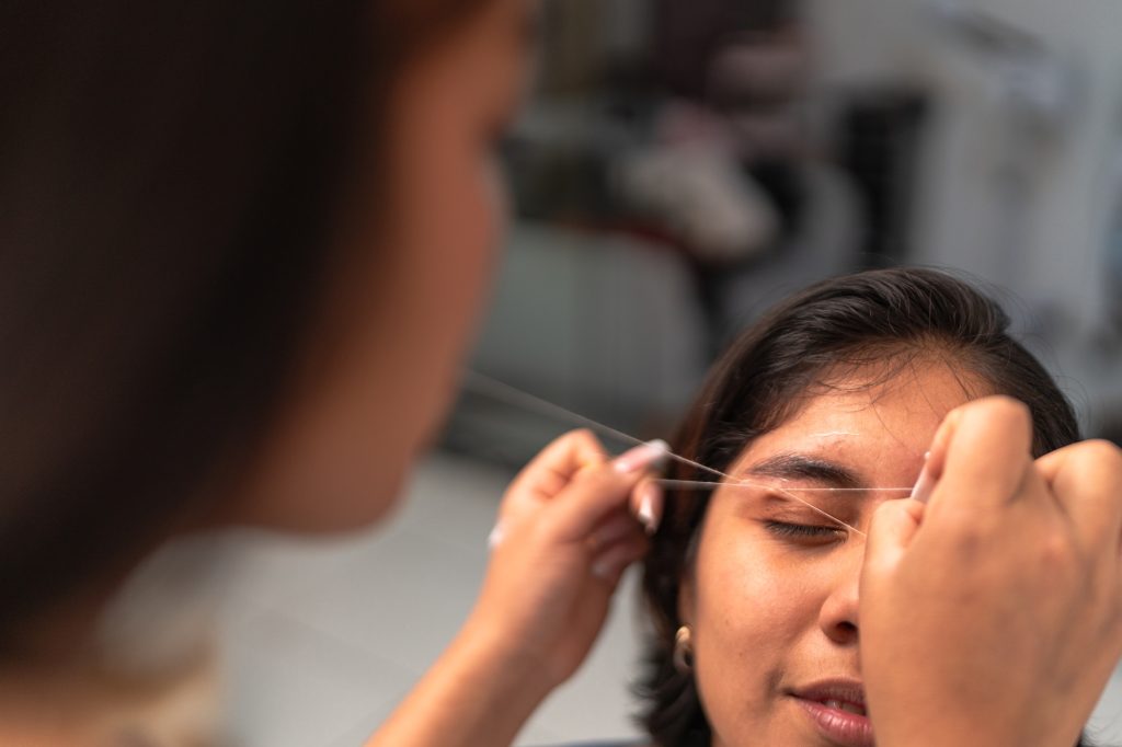 Beautician shaping eyebrows with thread close up