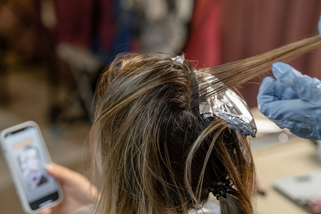 Girl getting hair colored in a salon while checking her phone for style inspiration