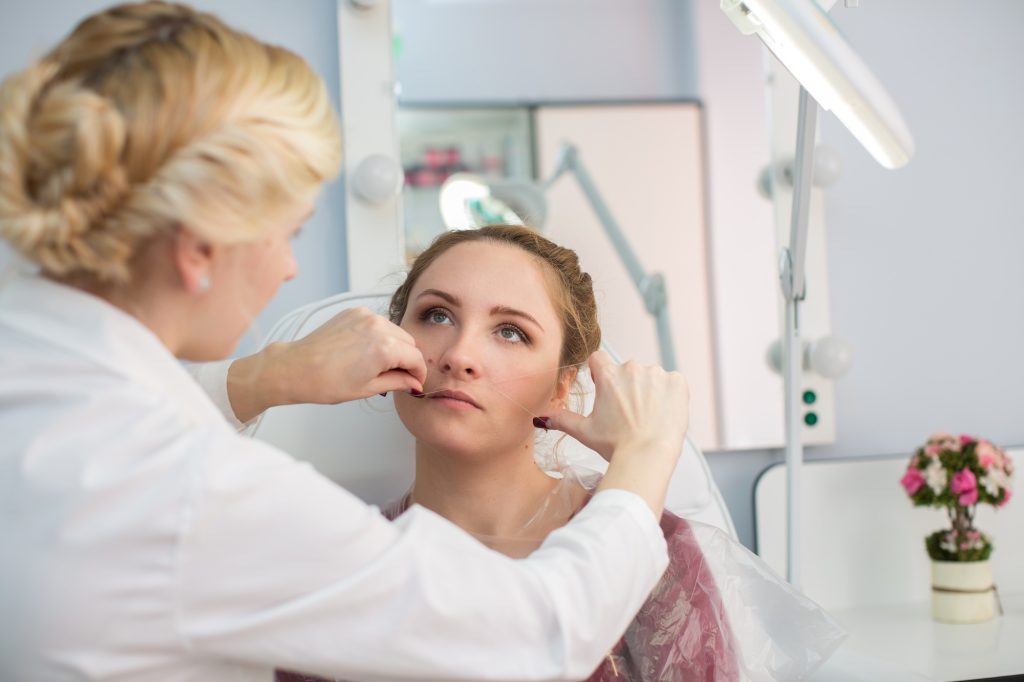Master corrects makeup, gives shape and thread plucks eyebrows in a beauty salon.